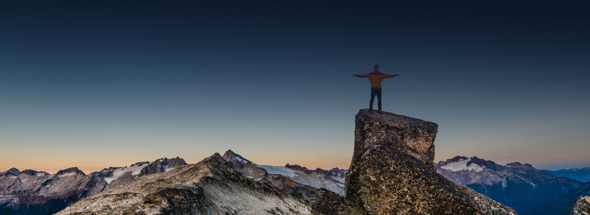 man wearing a yellow jersey standing on a rock looking out onto mountains